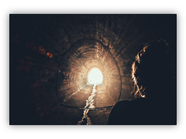 A woman walking through a tunnel towards the light.