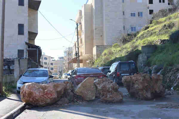 A street blocked with large boulders, cars parked along the side, and buildings on both sides under a clear sky.

"They created a separate road for settlers, a security road, so there wouldn't be Arabs on it." 

A stone barricade at one of the entrances to Beit Jala 

(Photo: Yuval Avraham)