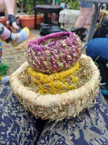 Three coil baskets of different sizes made with coils of dried hay and different colours of raffia stacked one inside the other