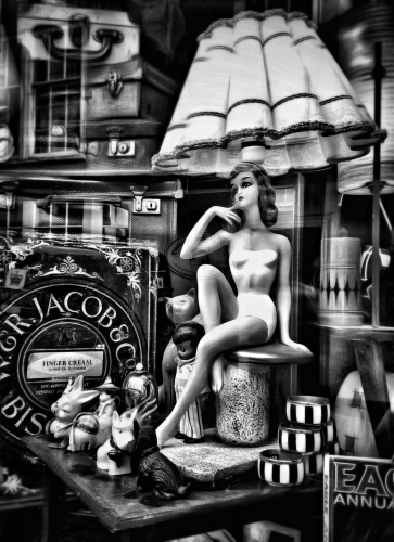 A black and white photo of a vintage shop window. In the window you see many vintage items from days gone by.