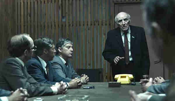 Screenshot from the miniseries Chernobyl, showing an elderly man speaking to a roomful of male political and industrial leaders.
